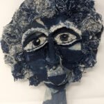 Textile sculpture by Emily-Kate Niskey featuring a hand-sewn face made from blue denim fabric, with textured curly hair, stitched eyes, a nose, and lips.